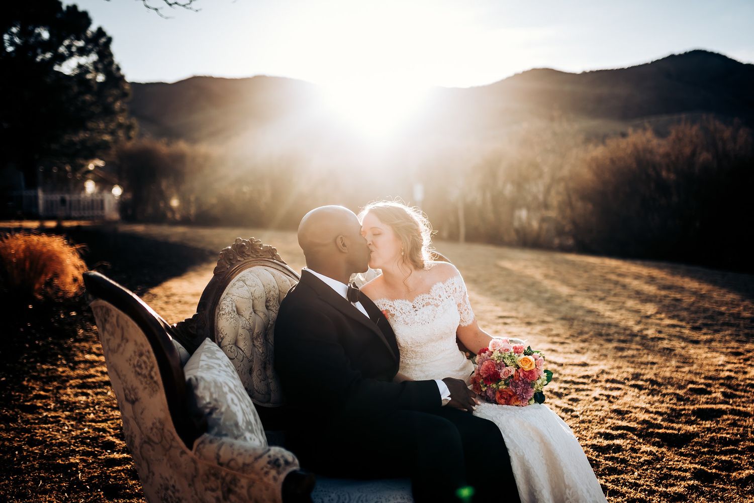 Wedding couple shares intimate moment on vintage couch during golden hour mountain sunset.