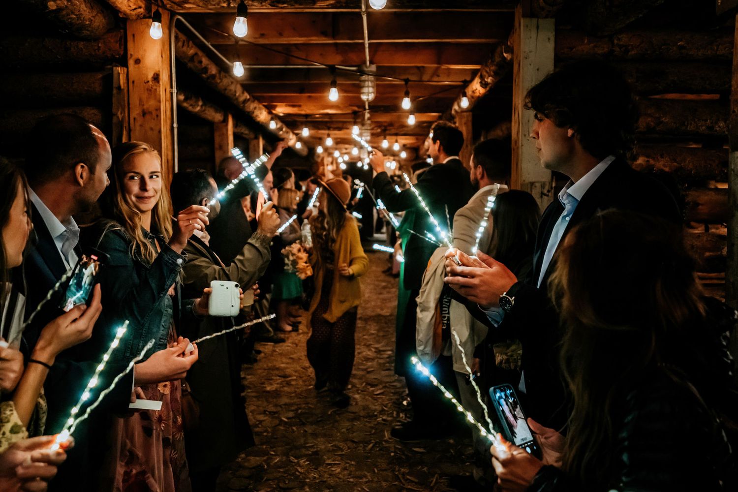 Wedding guests holding glowing blue light sticks in a rustic indoor venue.