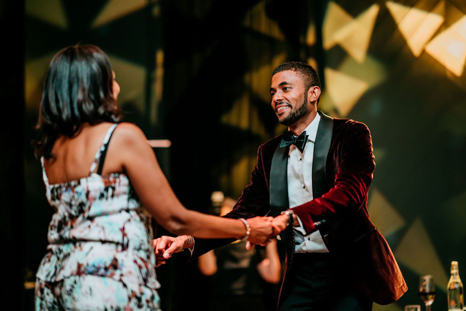 Couple sharing a playful dance moment at a formal reception with decorative lighting effects.