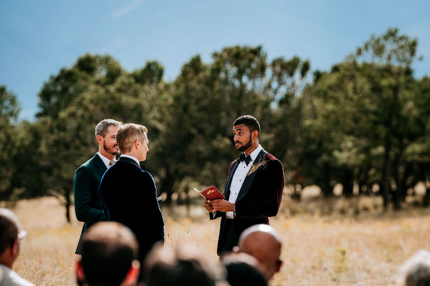 Intimate wedding ceremony taking place in a rustic outdoor setting with guests watching.