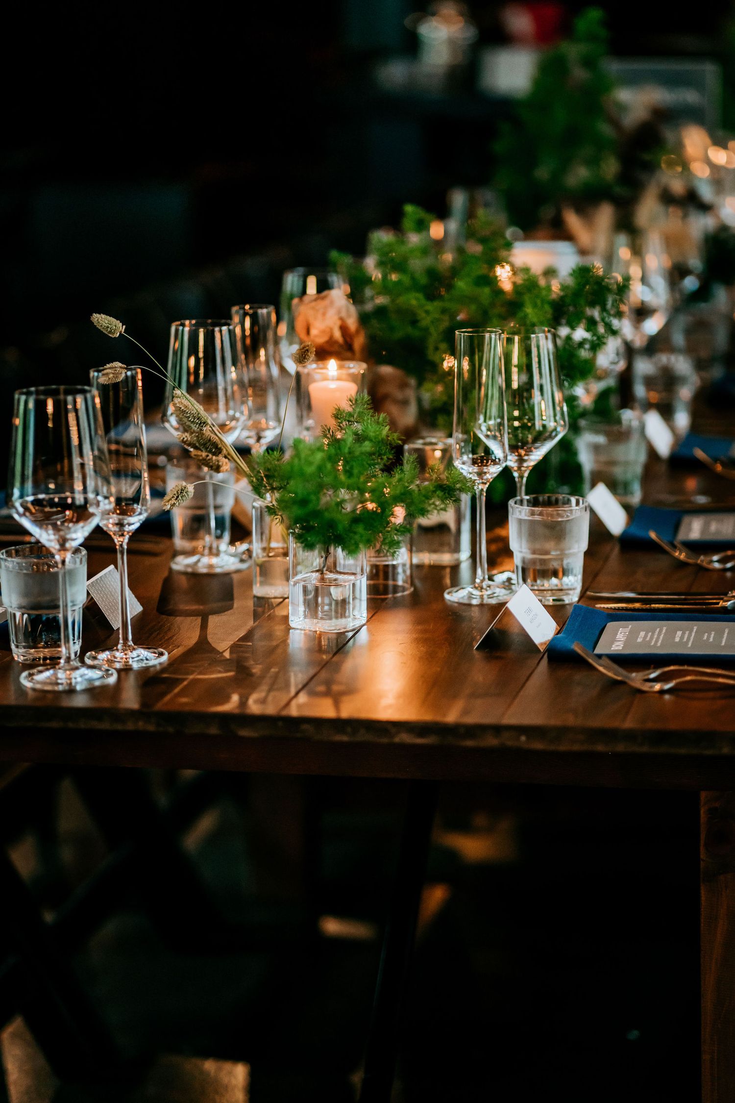 Elegant wedding table setting with wine glasses, greenery, and candlelight decorations.
