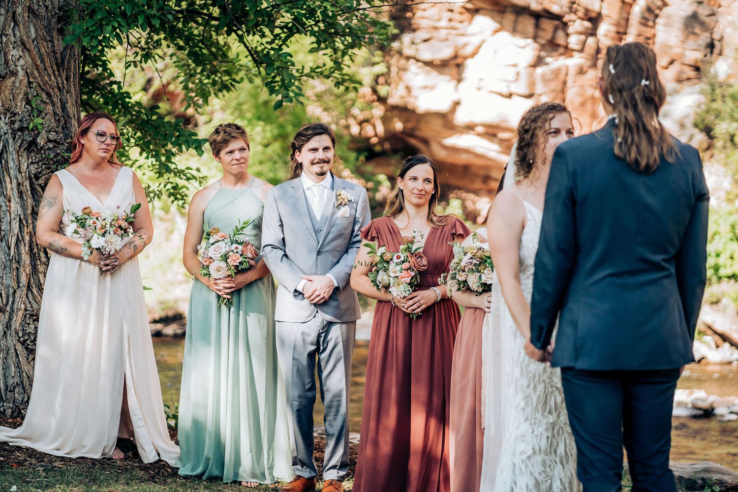 Wedding party lineup with bridesmaids in mix-matched pastel dresses holding bouquets.
