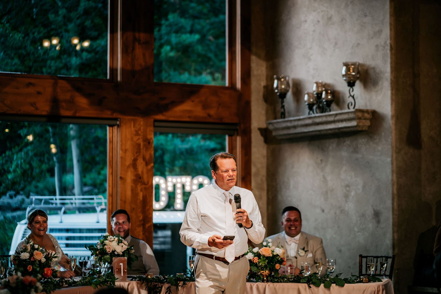 Speaker in white giving a toast at an elegant rustic wedding reception venue.