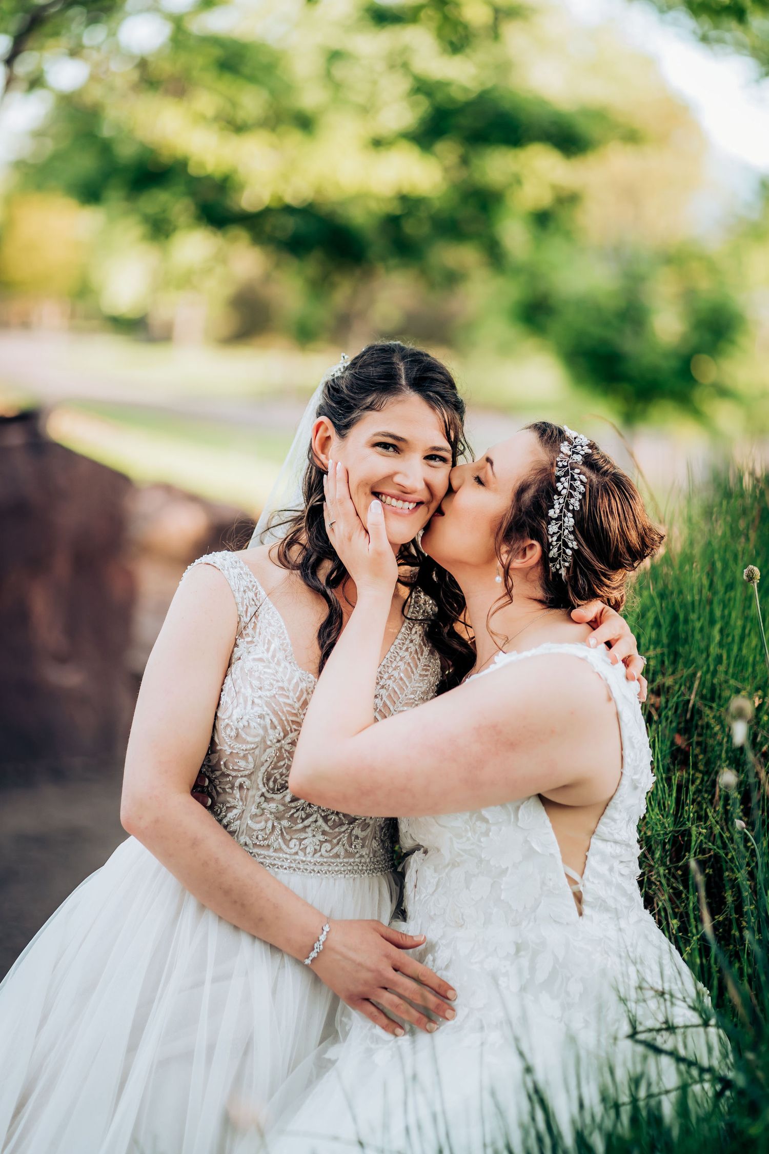 Joyful wedding couple embracing and laughing together in elegant white gowns outdoors.