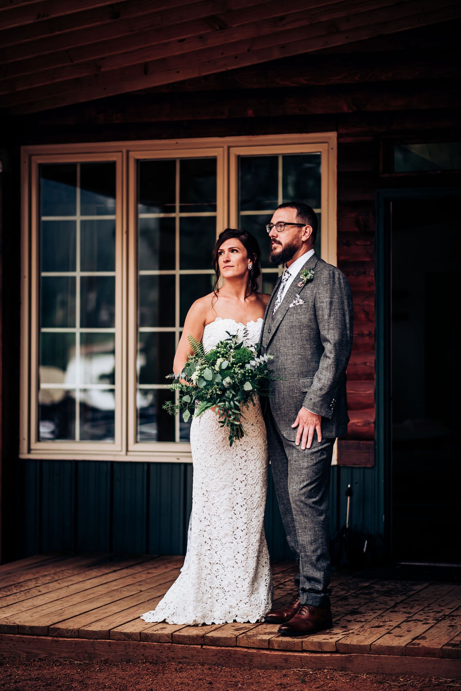 Bride and groom pose together on wooden porch of rustic cabin venue.