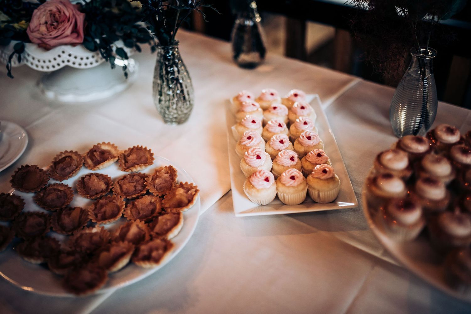 Dessert table at a wedding reception featuring chocolate cookies and pink frosted pastries.