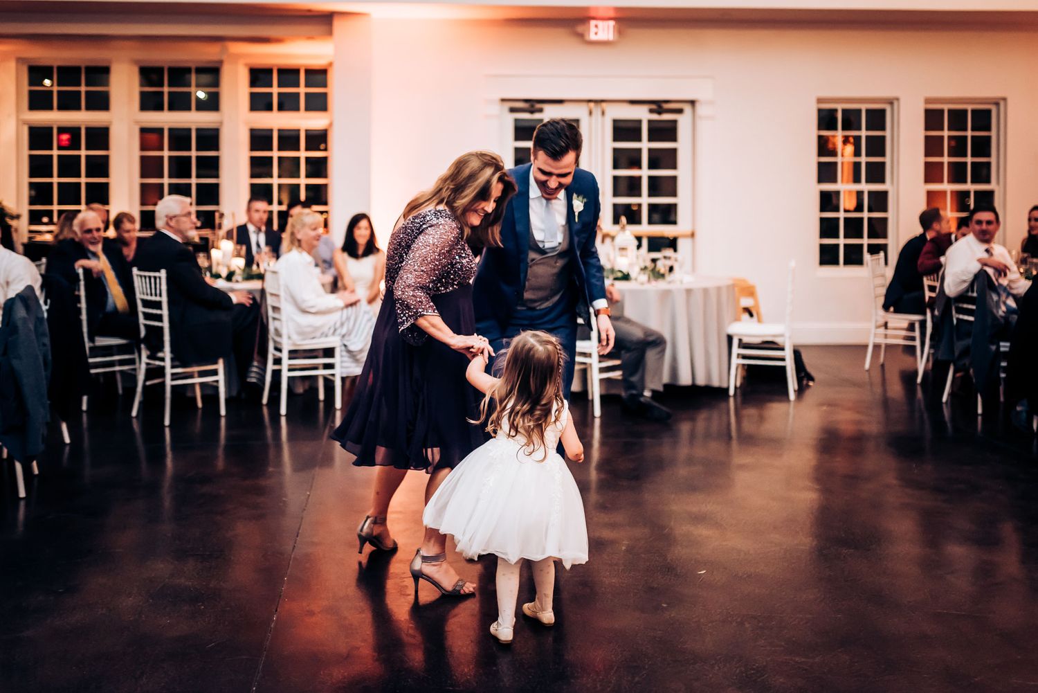 Family dances together at wedding reception with young flower girl in white dress.