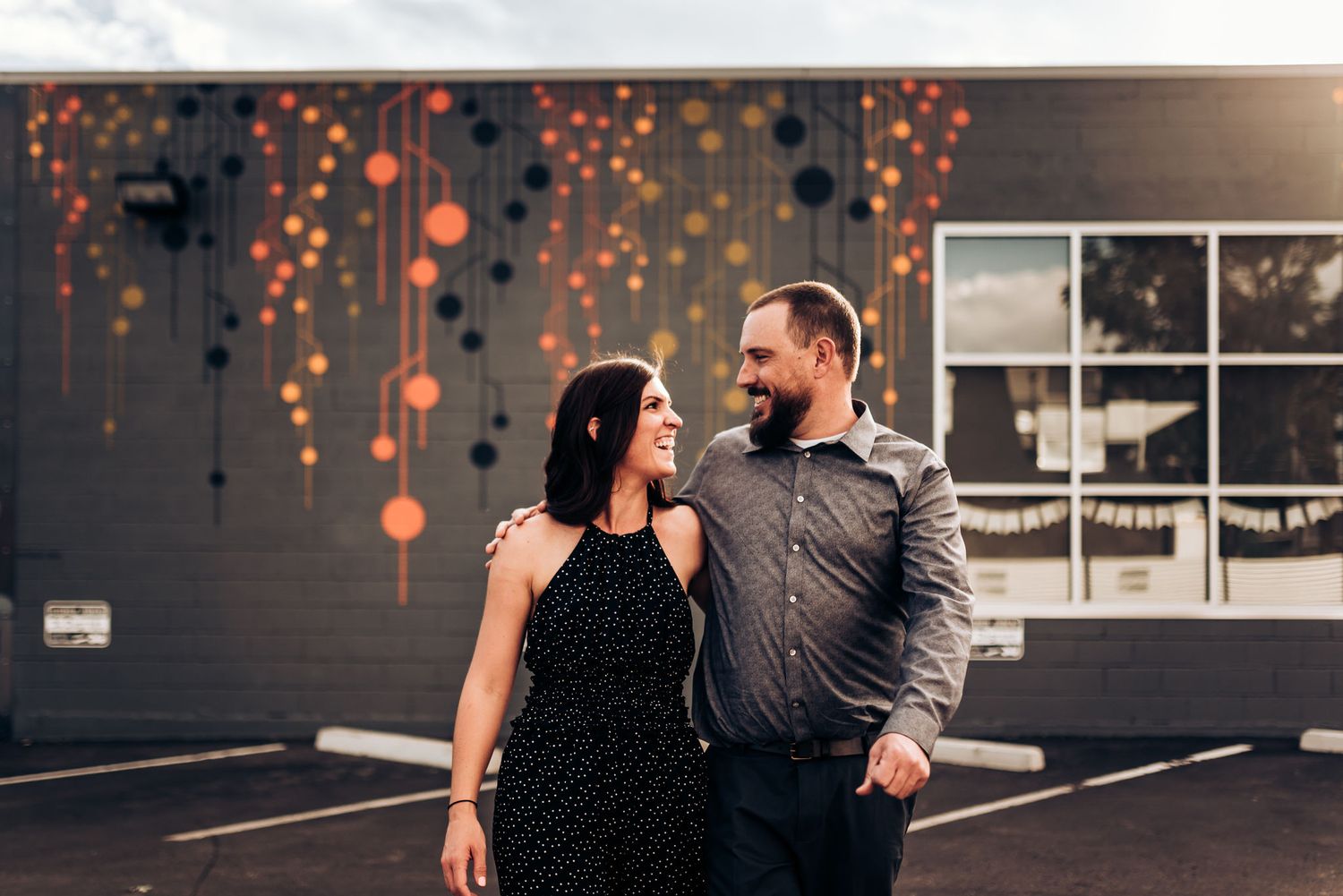 A couple shares a romantic moment against a wall with glowing orange bokeh lights.