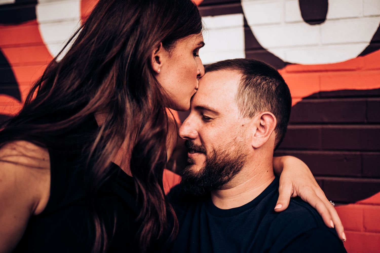 Intimate couple sharing a tender moment against a red background.