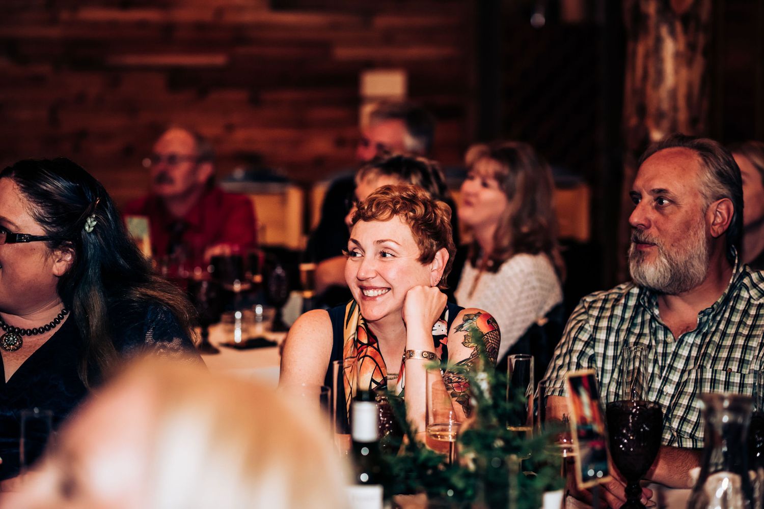 Guests laughing and enjoying themselves during a reception at a rustic wooden venue with warm lighting.