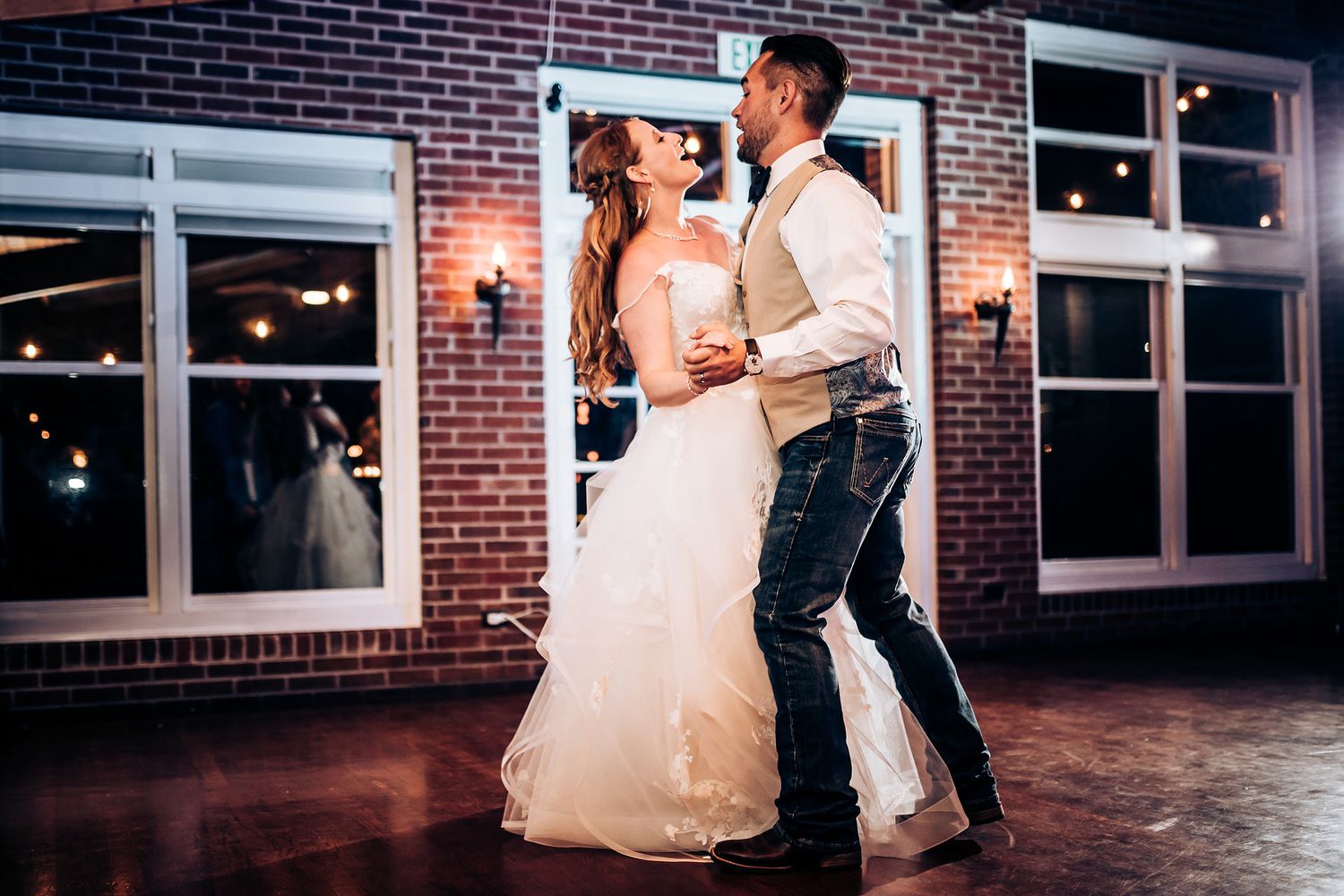 Couple dancing together in a rustic reception venue with large windows and exposed brick.