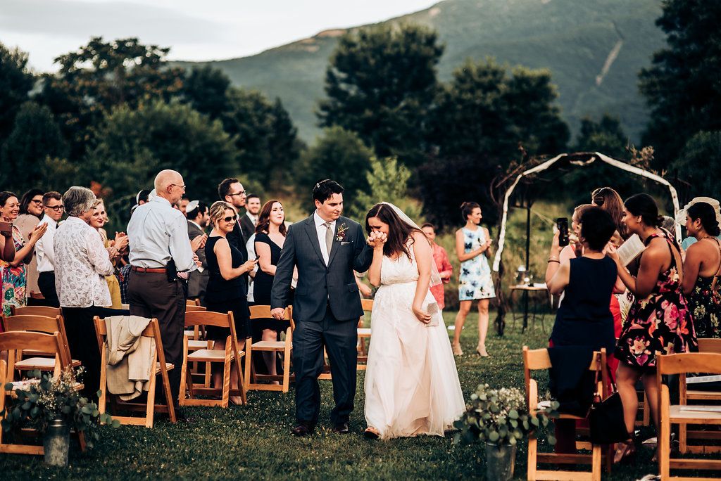 Wedding celebration in progress with guests standing and seated outdoors against mountain backdrop.