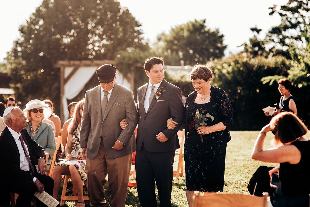Guests walk down an outdoor aisle during a sunny afternoon wedding ceremony.