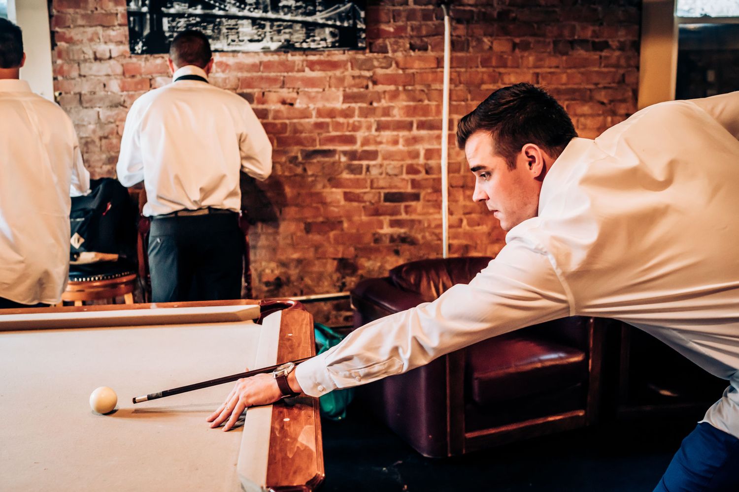 Person in white shirt playing pool at rustic brick-walled venue.
