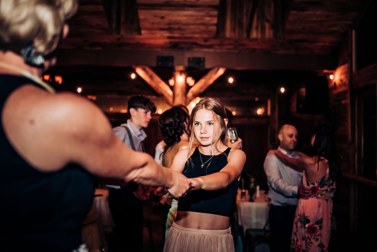 Lively dance floor scene at rustic wedding reception with wooden interior.