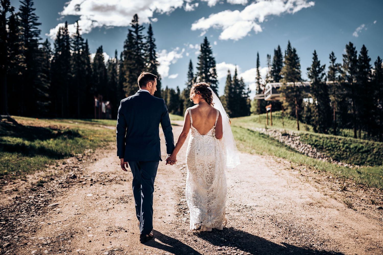 A couple holds hands while walking down a scenic mountain path on their wedding day.