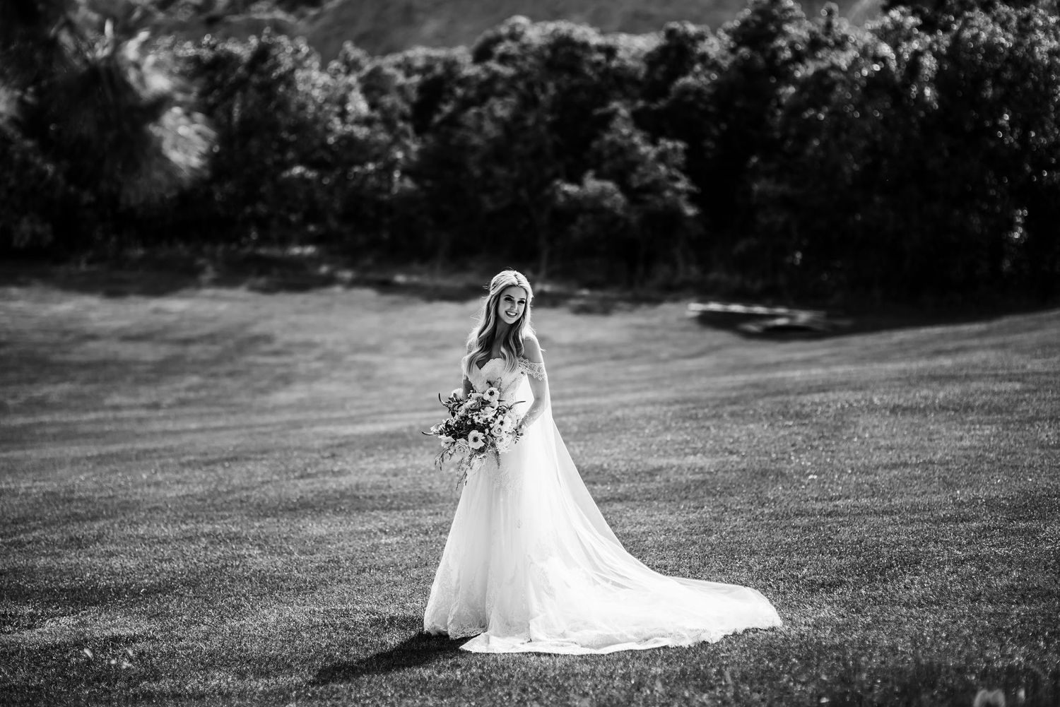 Dramatic black and white portrait of bride holding bouquet in open field.