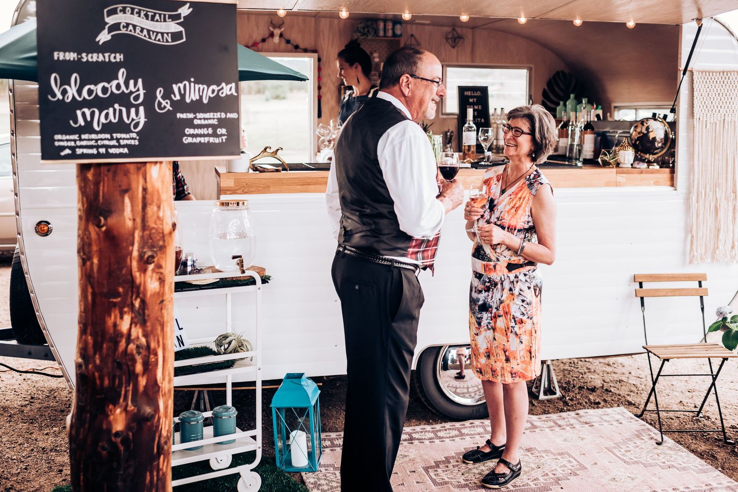 People chatting at a casual outdoor event with a chalkboard menu in the background.