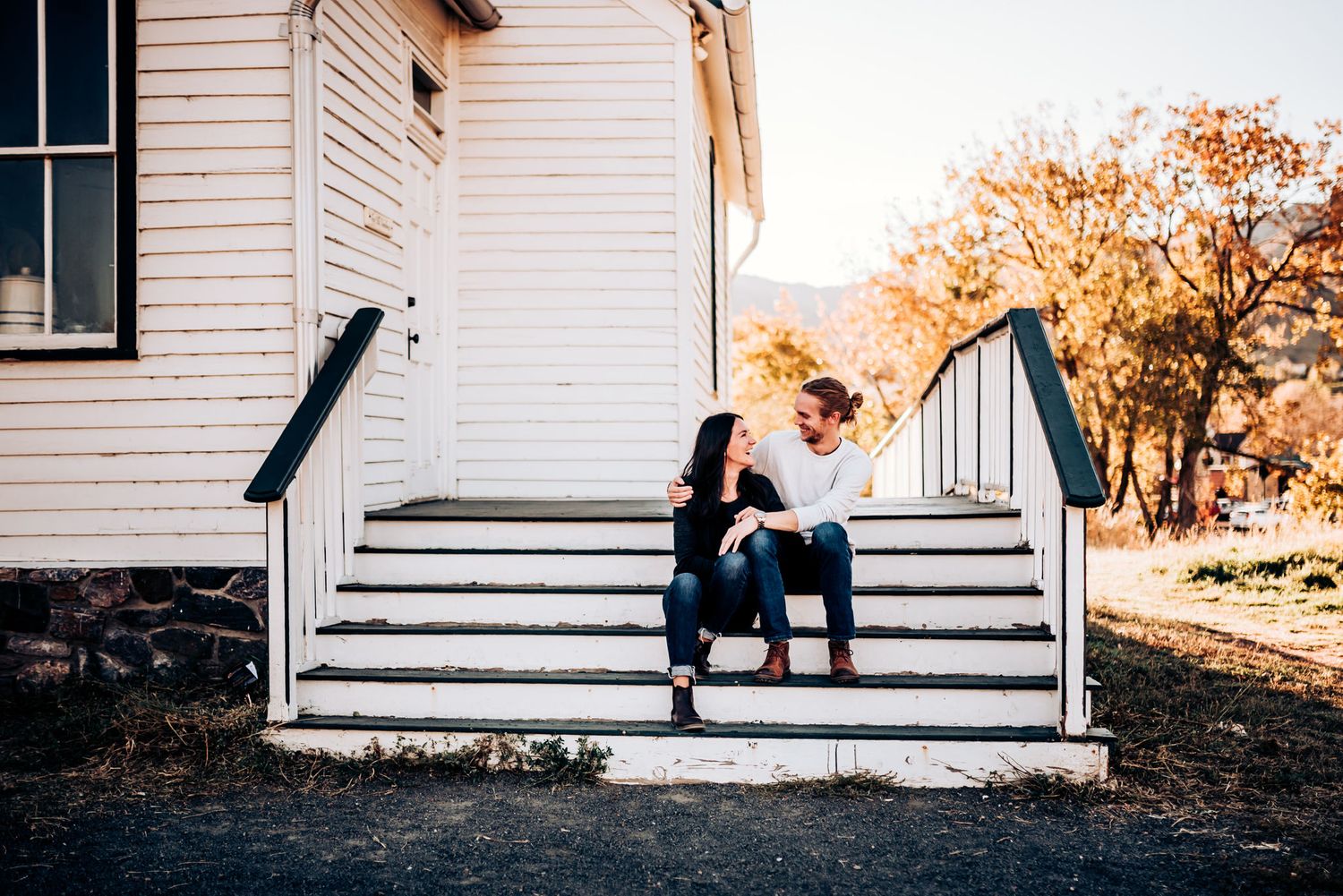 A couple sits on white steps of a house during golden autumn hours.