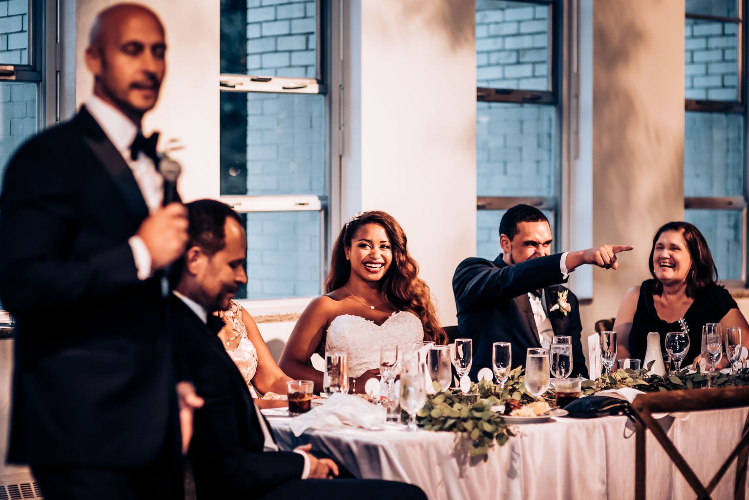 Wedding reception speech moment with formal attire guests at decorated dining tables.