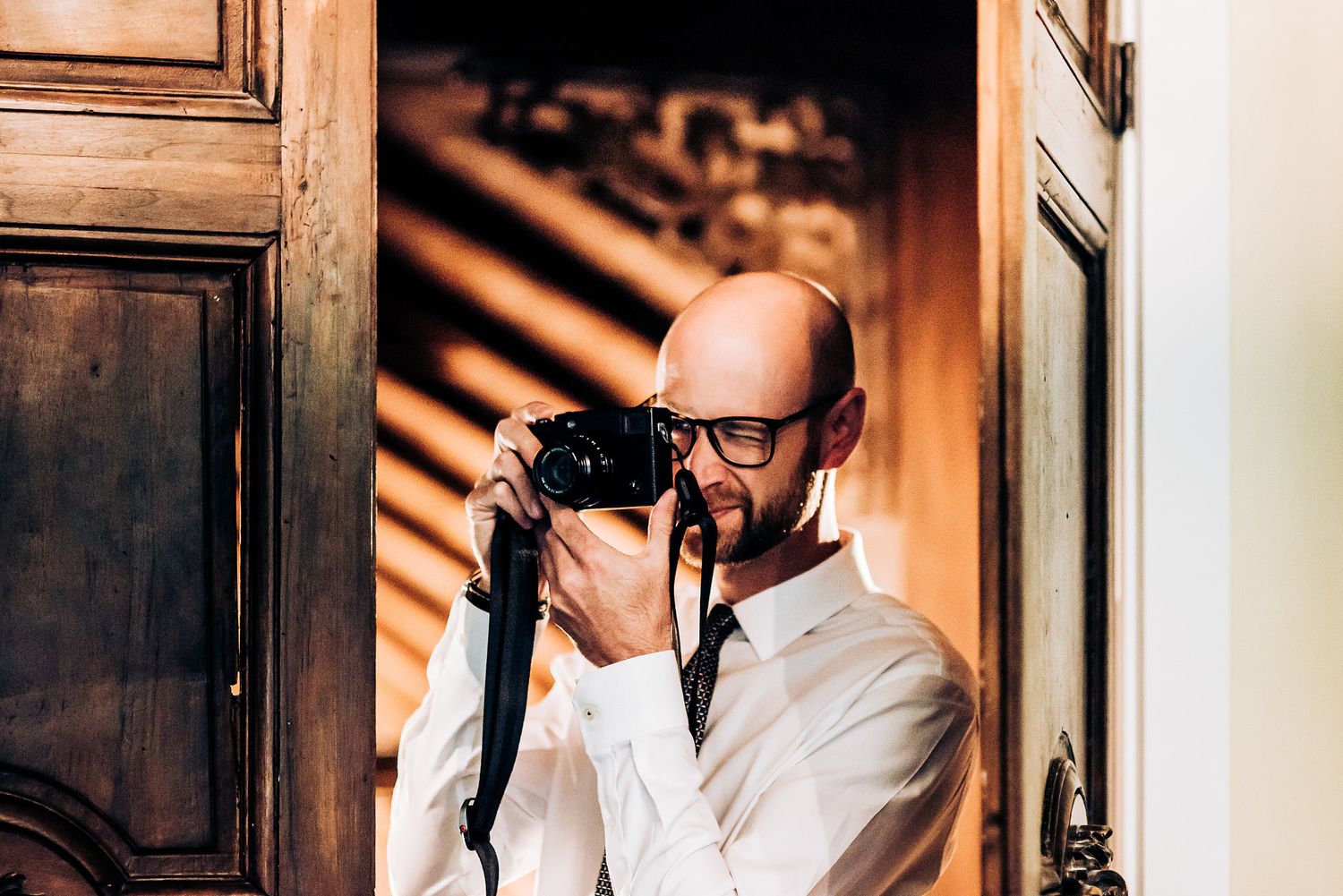 Wedding photographer in white shirt capturing moments through professional camera.