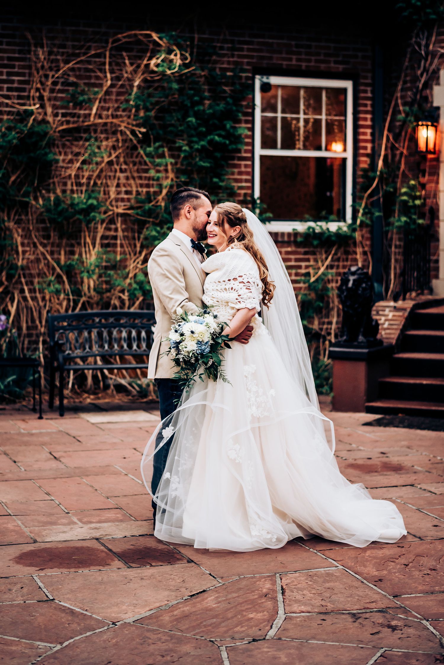 Romantic wedding portrait against brick wall with climbing vines and vintage architecture.