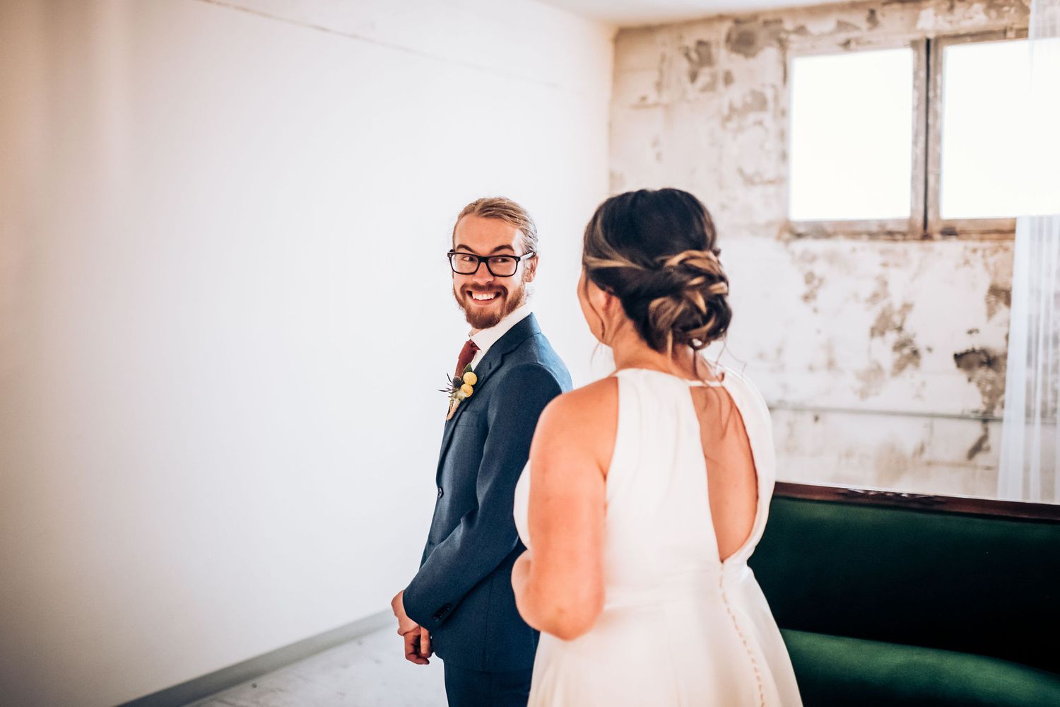 Couple shares first look moment in front of green sofa in minimalist white room.