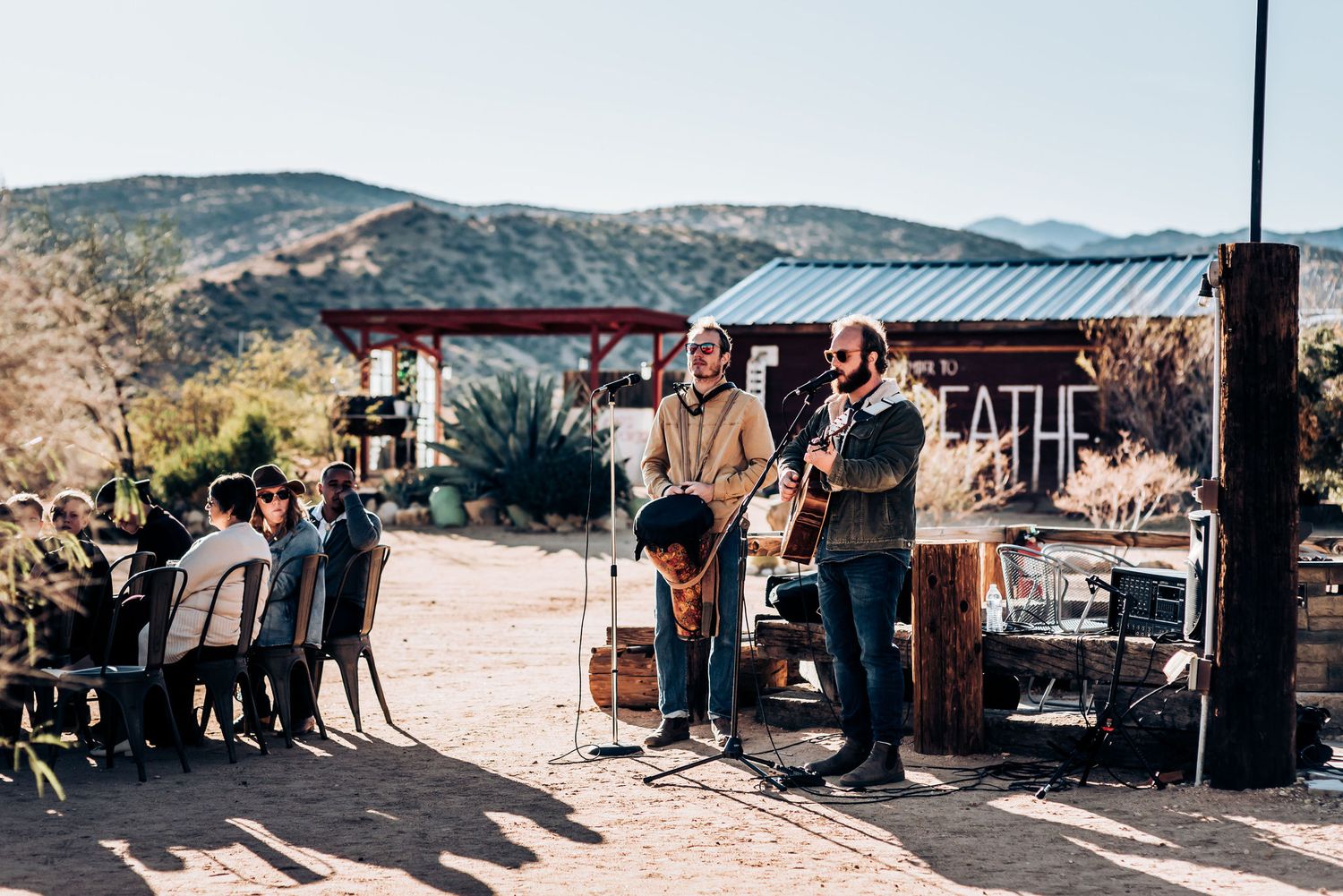 Musicians perform at an outdoor desert venue with mountains in the background.