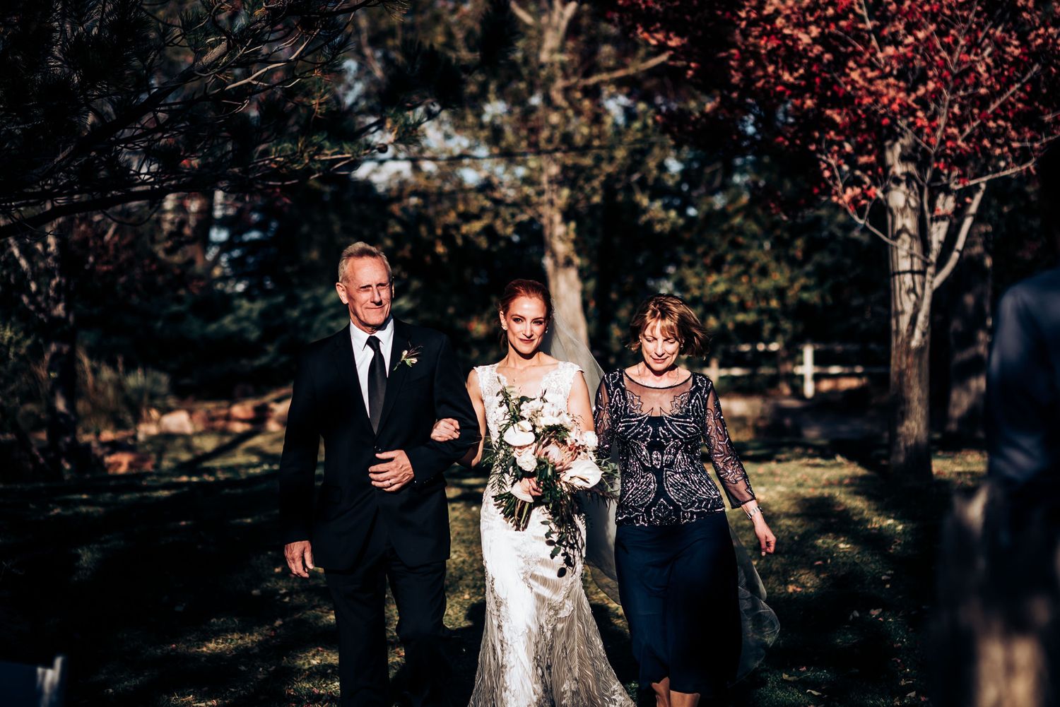 A beautiful outdoor wedding processional shows the bridal party walking through a garden setting with autumn trees.