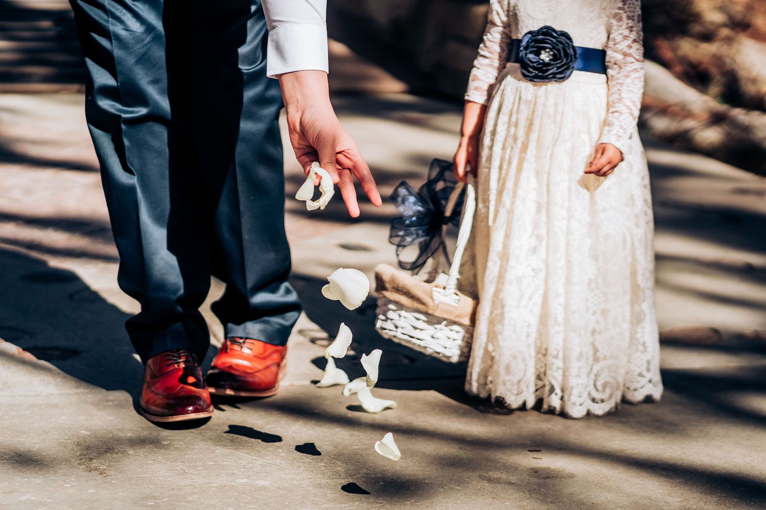 Close-up of flower petals scattered between formal shoes and white dress hem.