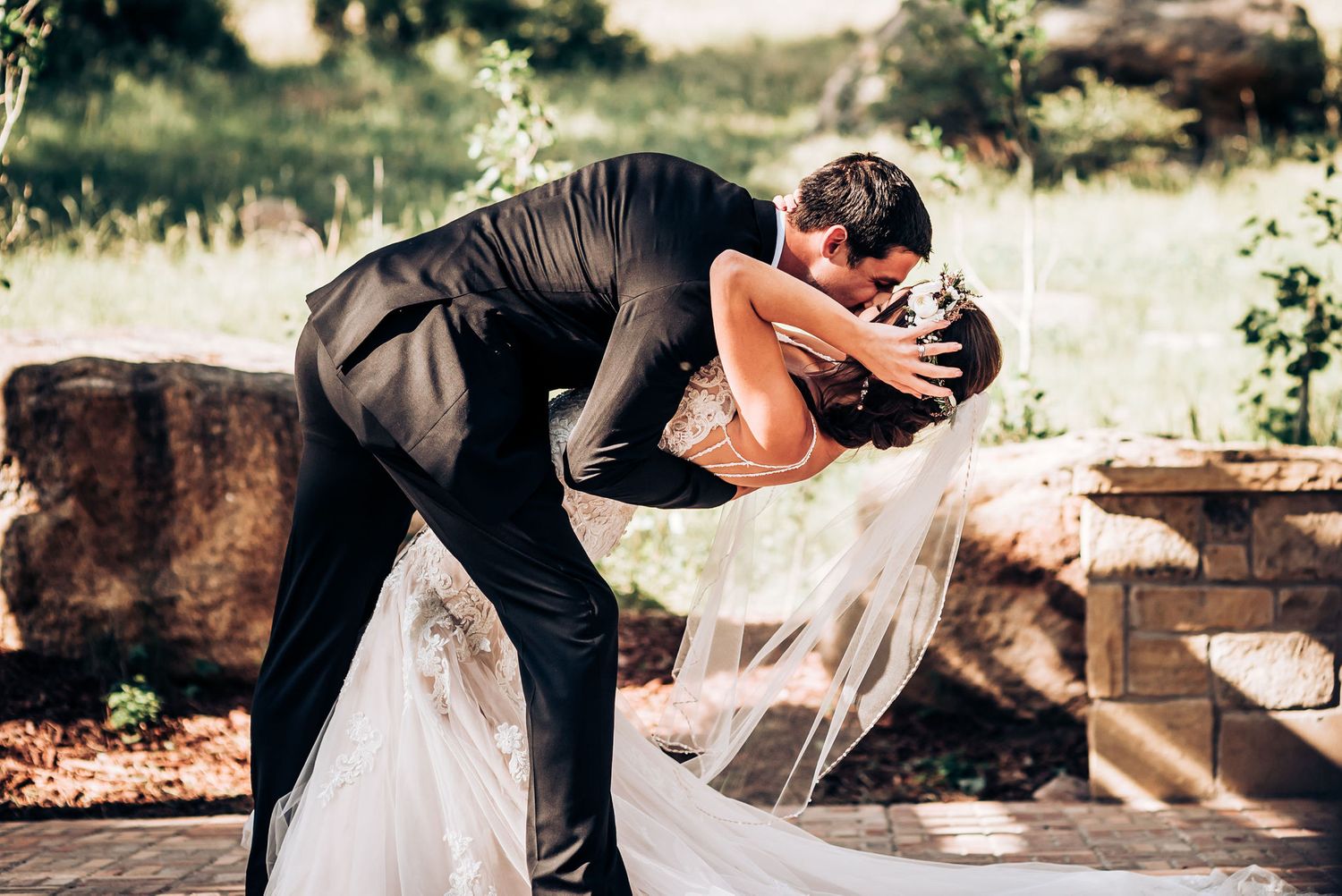 Dramatic wedding dip pose outdoors with flowing veil and natural scenery.