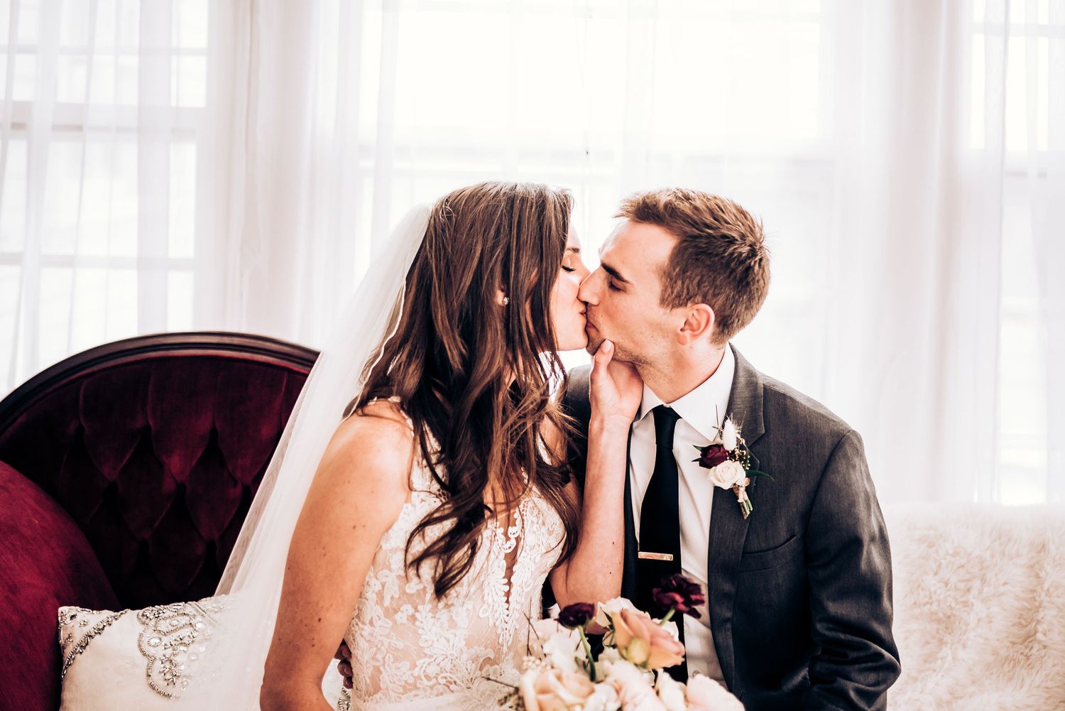 Tender wedding moment captured on burgundy vintage sofa.