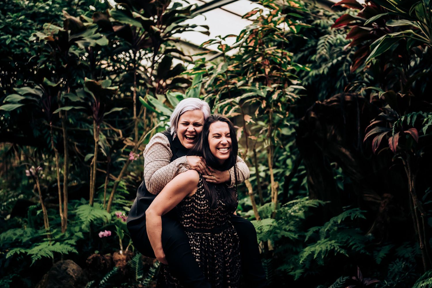 Two people share a playful piggyback ride in a tropical garden setting.