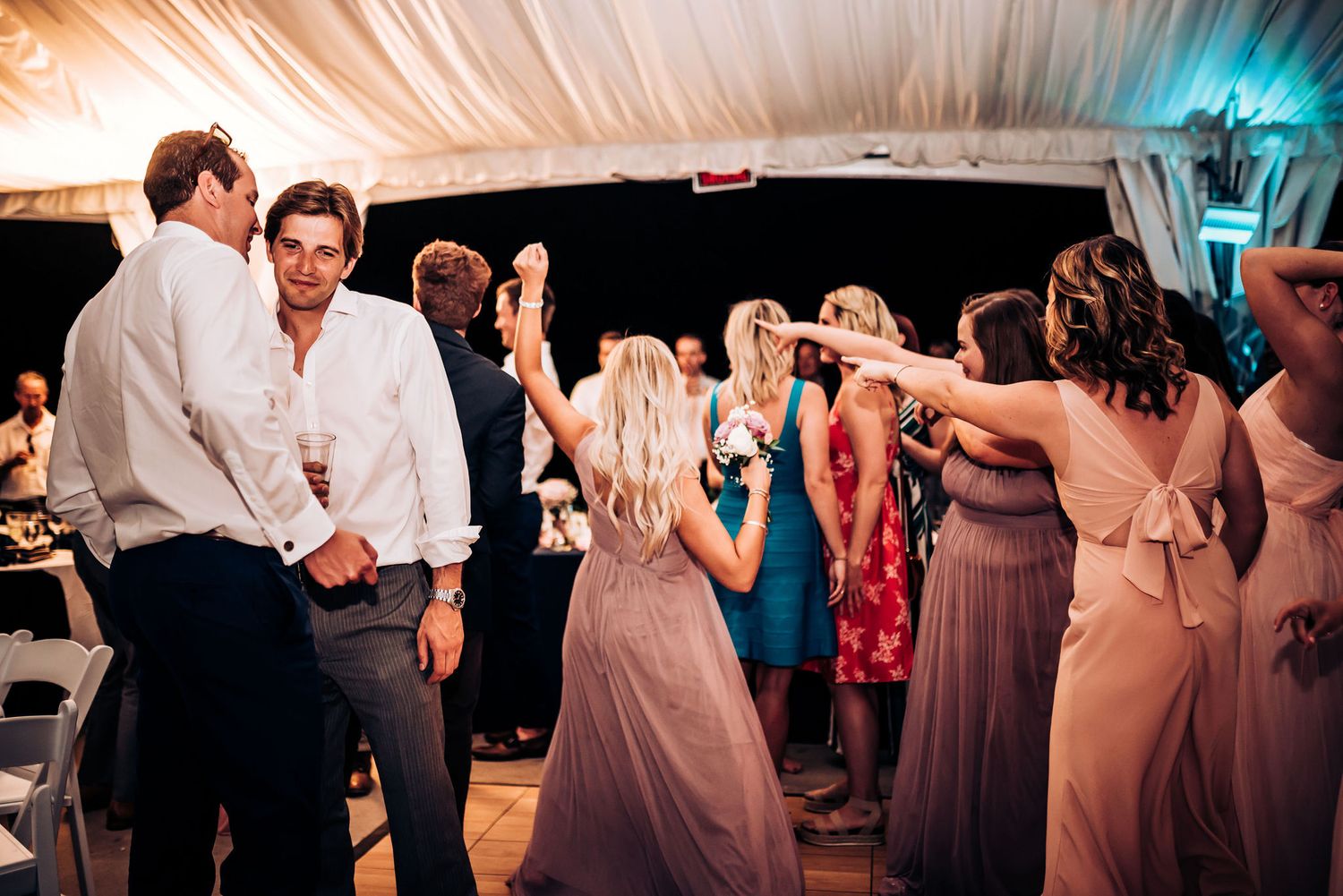 Dancing guests enjoy a lively wedding reception under elegant white tent draping.