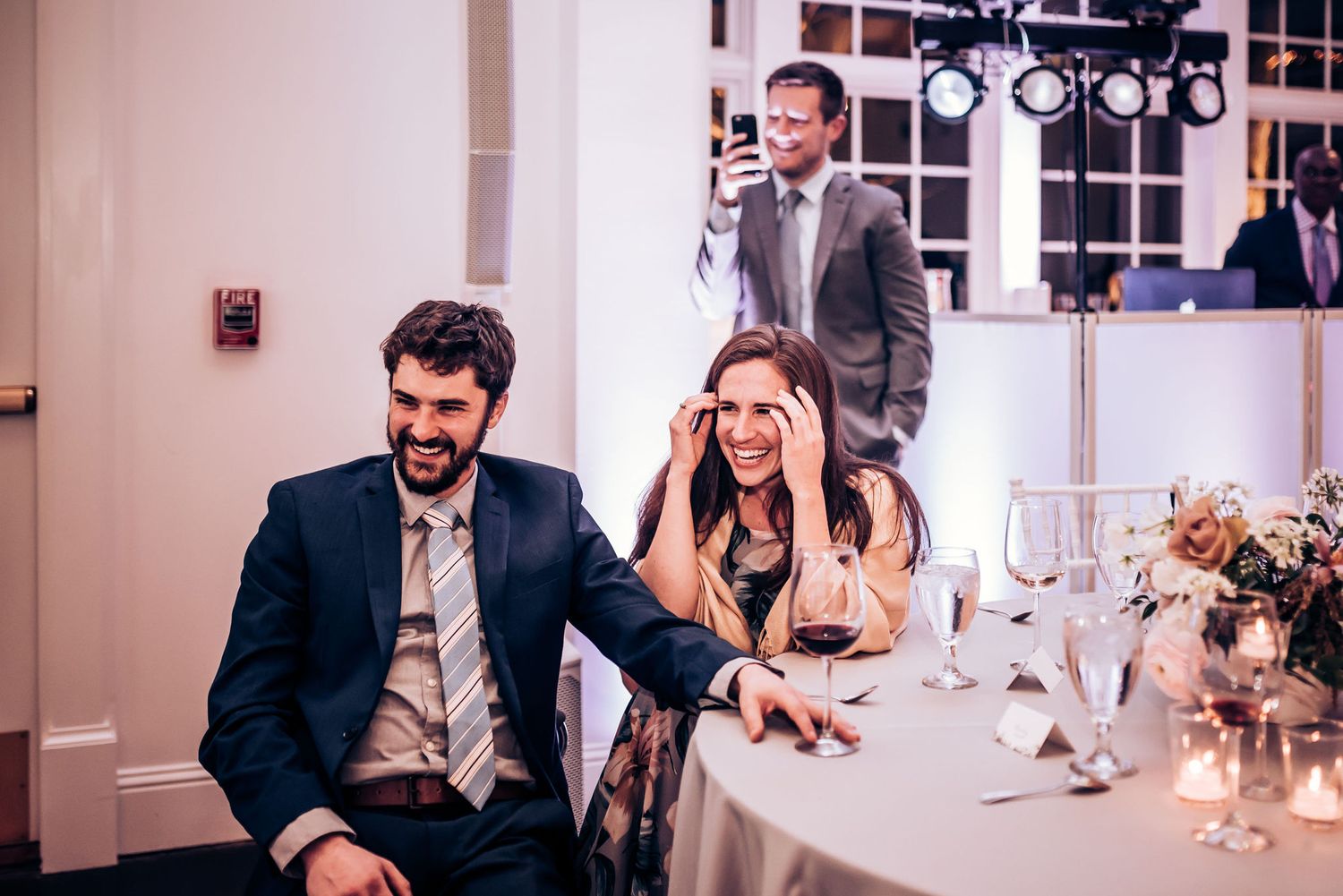 Wedding reception guests react emotionally to speeches at decorated table with candlelight.