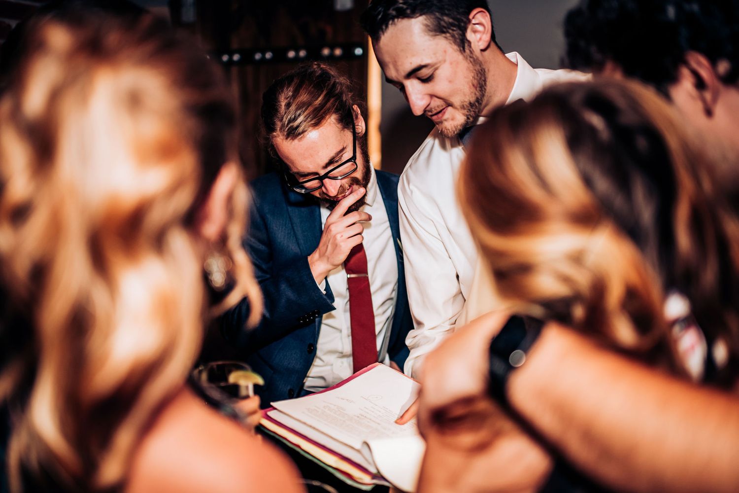 A group huddles together looking at a document during what appears to be a wedding celebration.