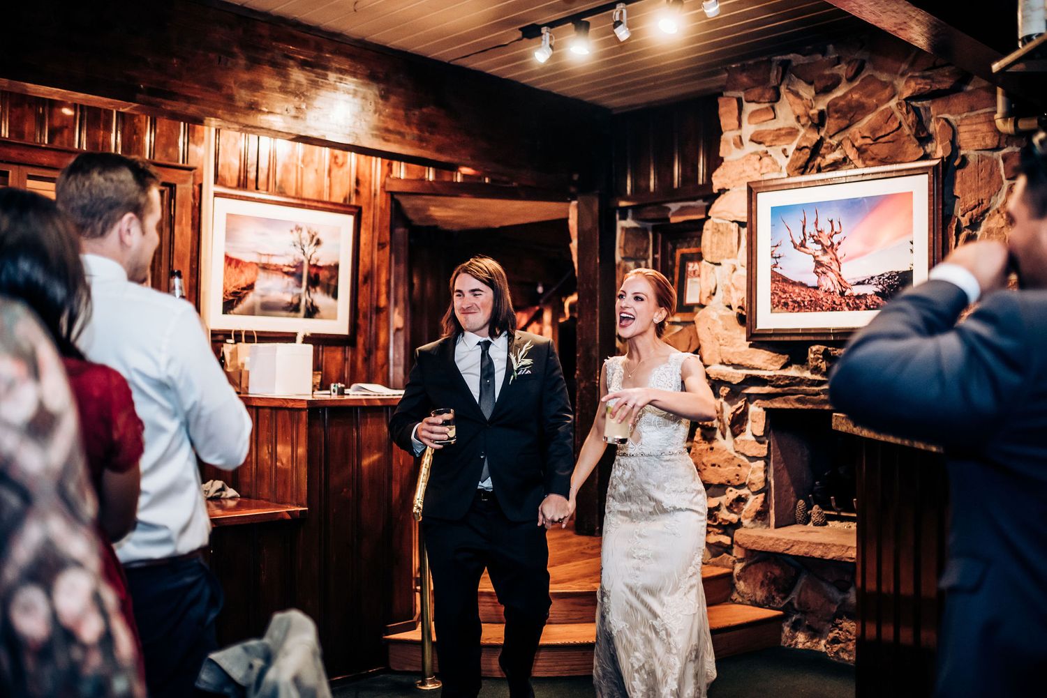 A couple shares their first dance in a rustic wood-paneled venue with onlookers.