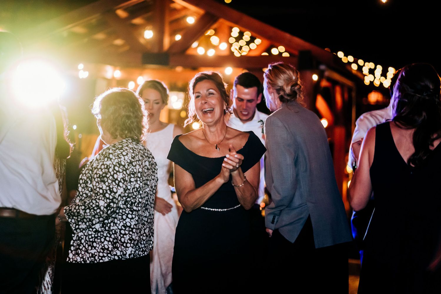 Guests dancing and celebrating at a nighttime wedding reception under warm string lights.