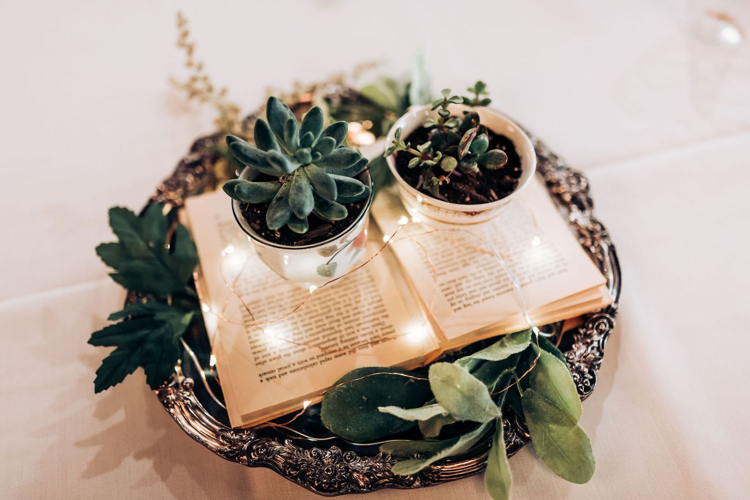 Succulents arranged on open vintage books with decorative tray as wedding decor.