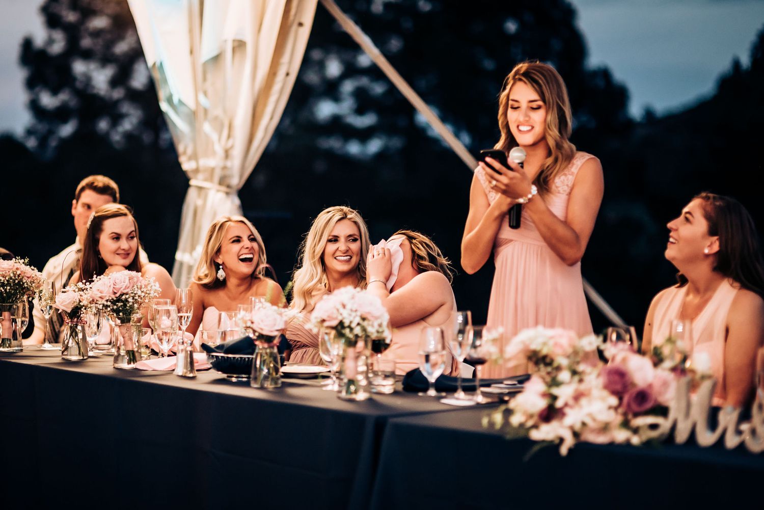 Bridesmaid delivering speech while standing at outdoor wedding reception.