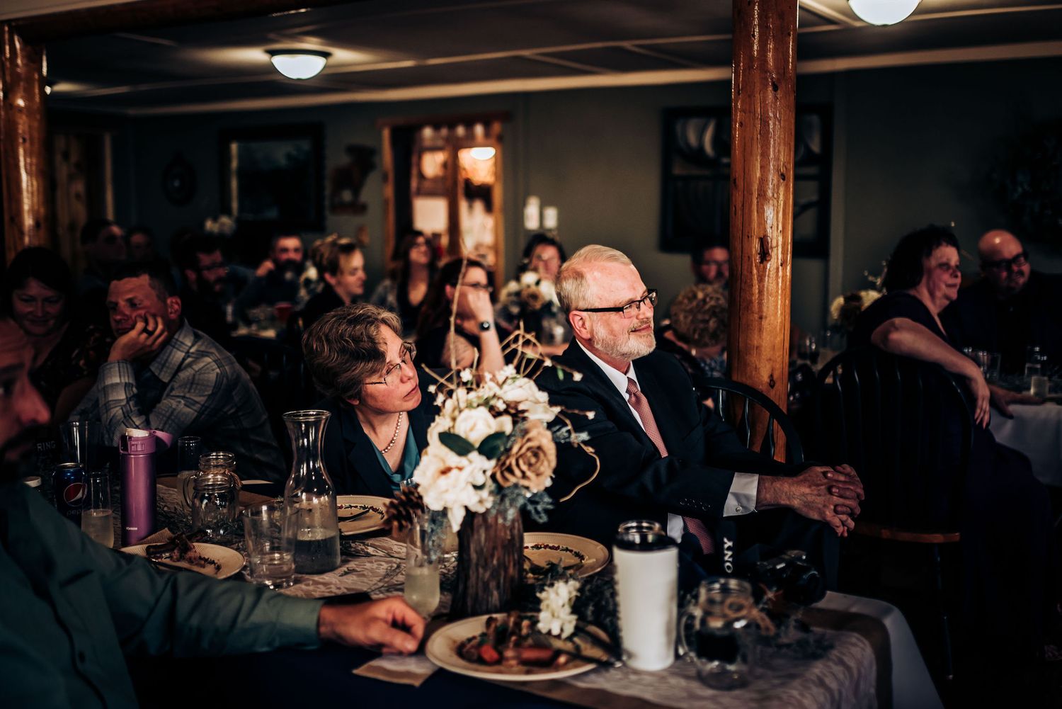 Guests seated at decorated tables during an indoor reception with rustic wooden beams.