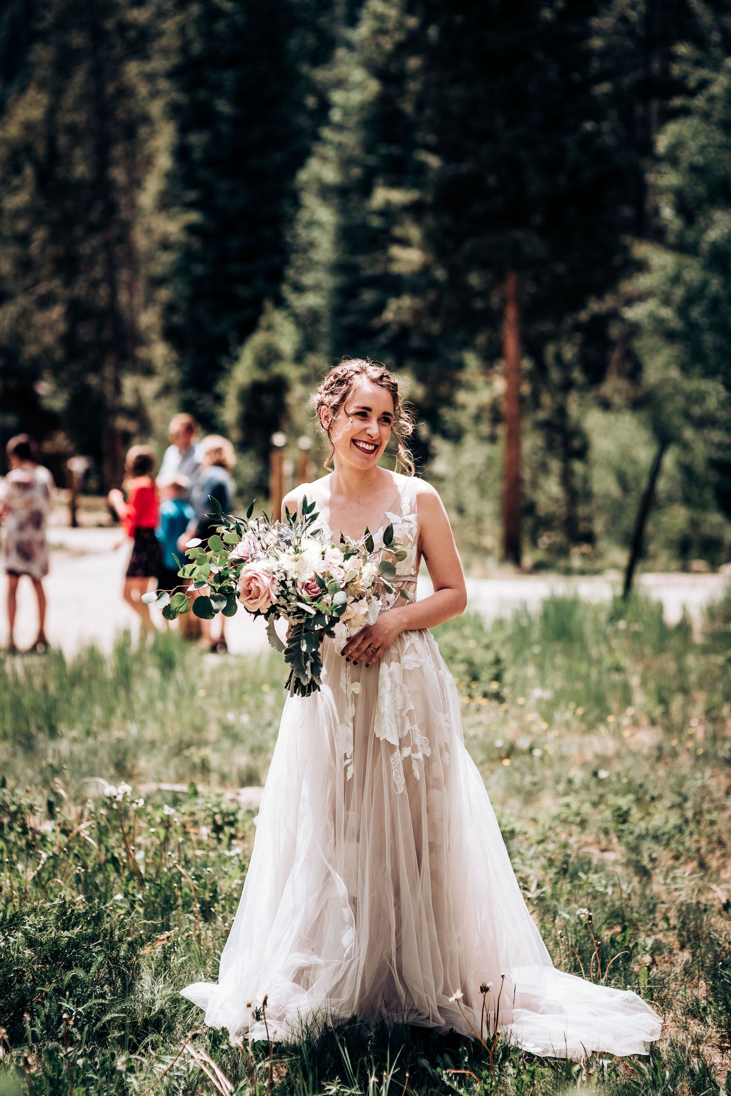 A joyful bride in a flowing champagne dress holds a wildflower bouquet in a mountain meadow.