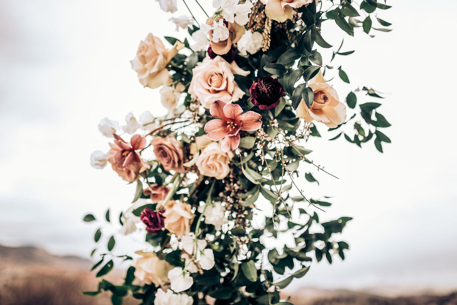 Lush floral wedding arch arrangement featuring peach roses and greenery against cloudy sky.