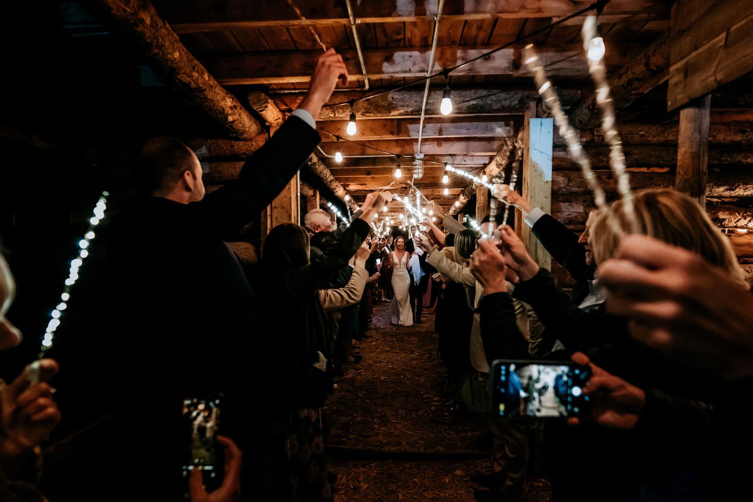 Guests forming a celebratory tunnel with glowing wands in a dimly lit rustic venue.