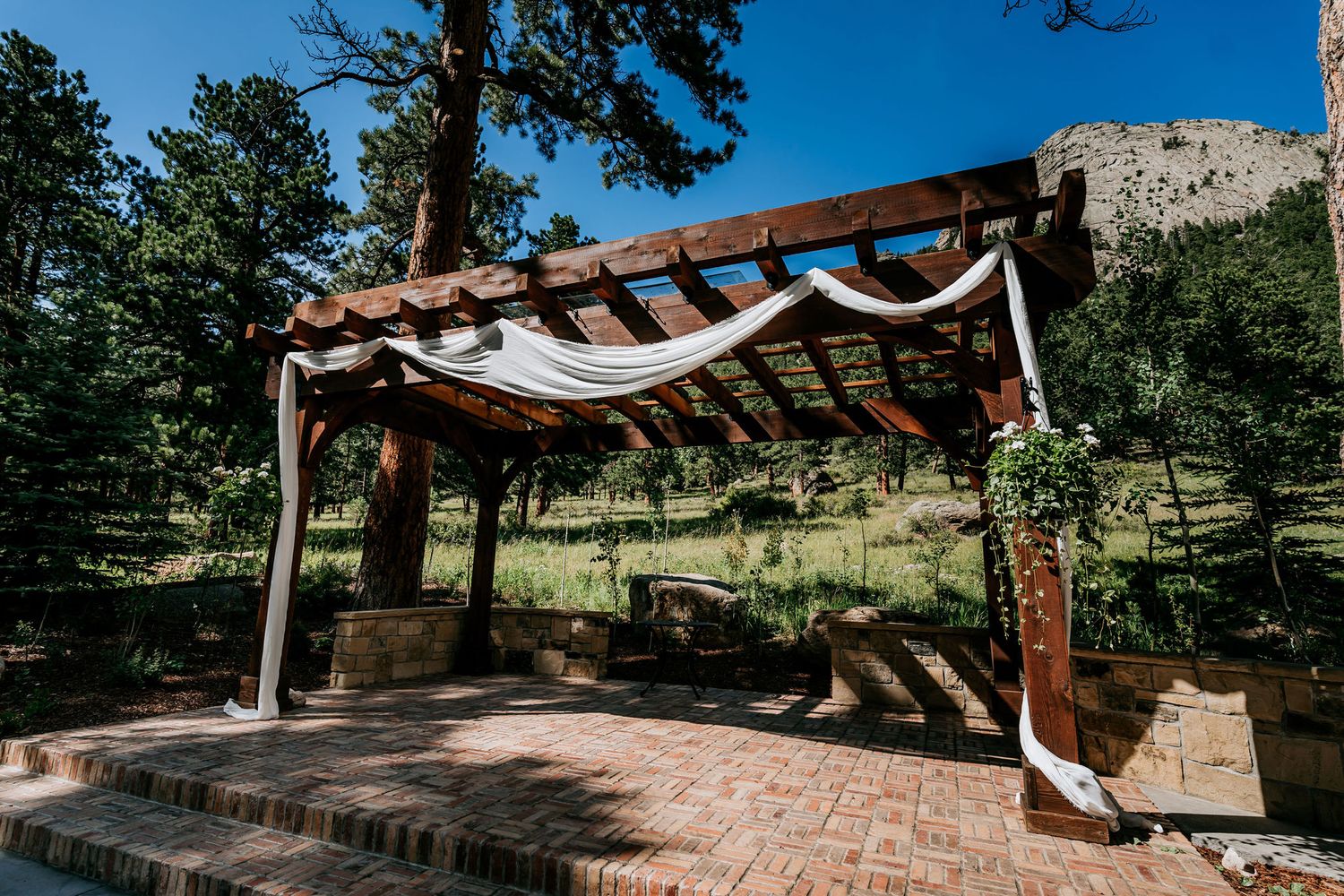 Rustic wooden pergola with white fabric draping in a mountain setting.