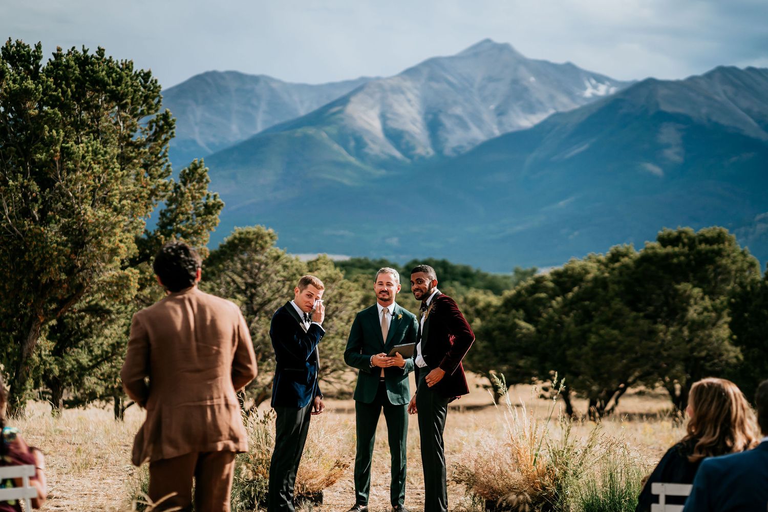 Small group gathered for outdoor wedding ceremony with dramatic mountain peaks in background.