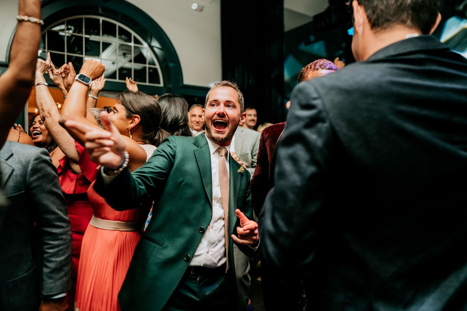 Energetic wedding reception celebration with guests dancing and celebrating in formal attire.