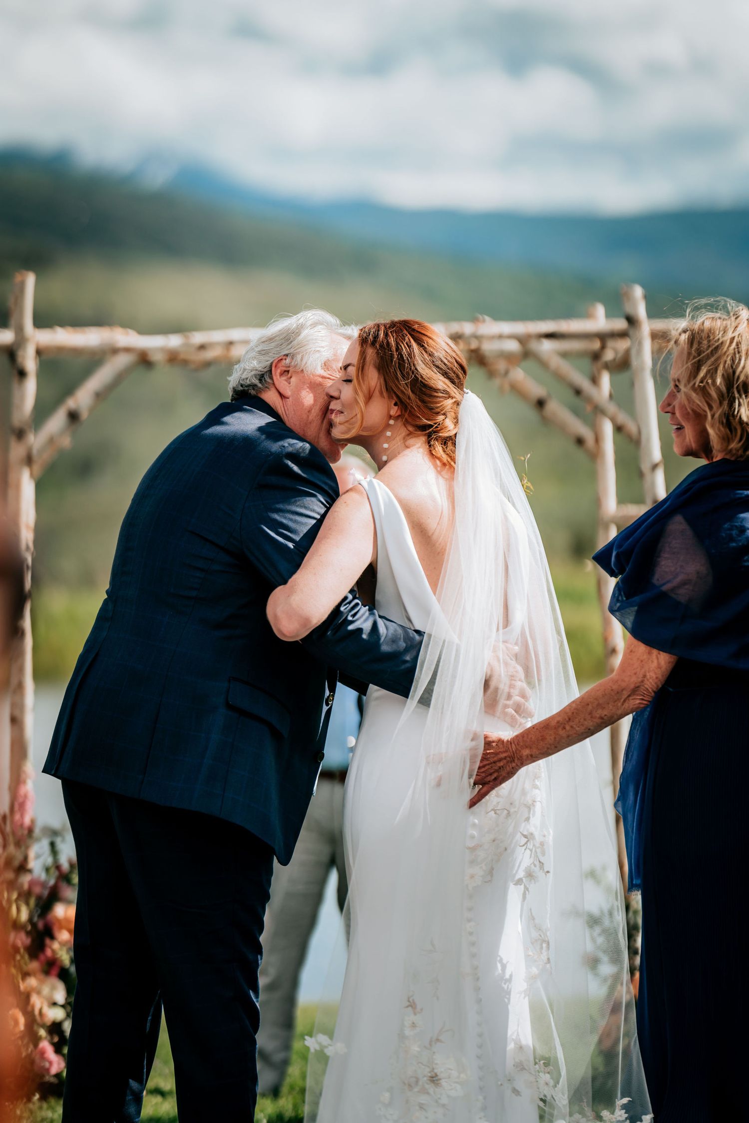 Emotional moment during mountain wedding ceremony under rustic wooden arch.