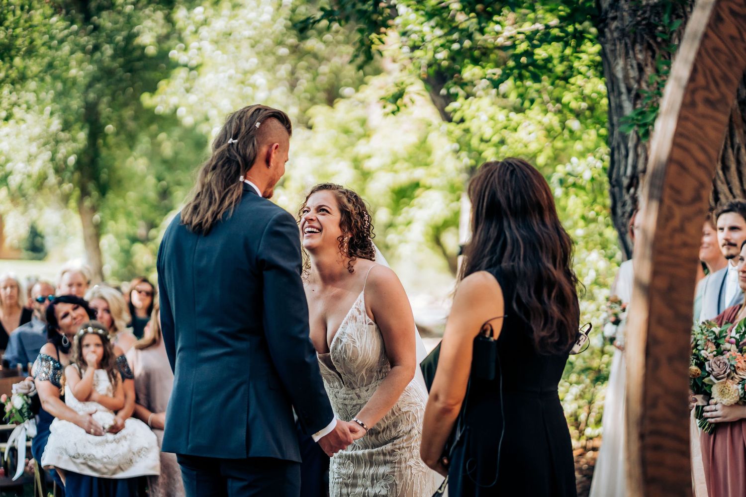 An outdoor wedding ceremony with guests seated under trees creating a natural canopy.