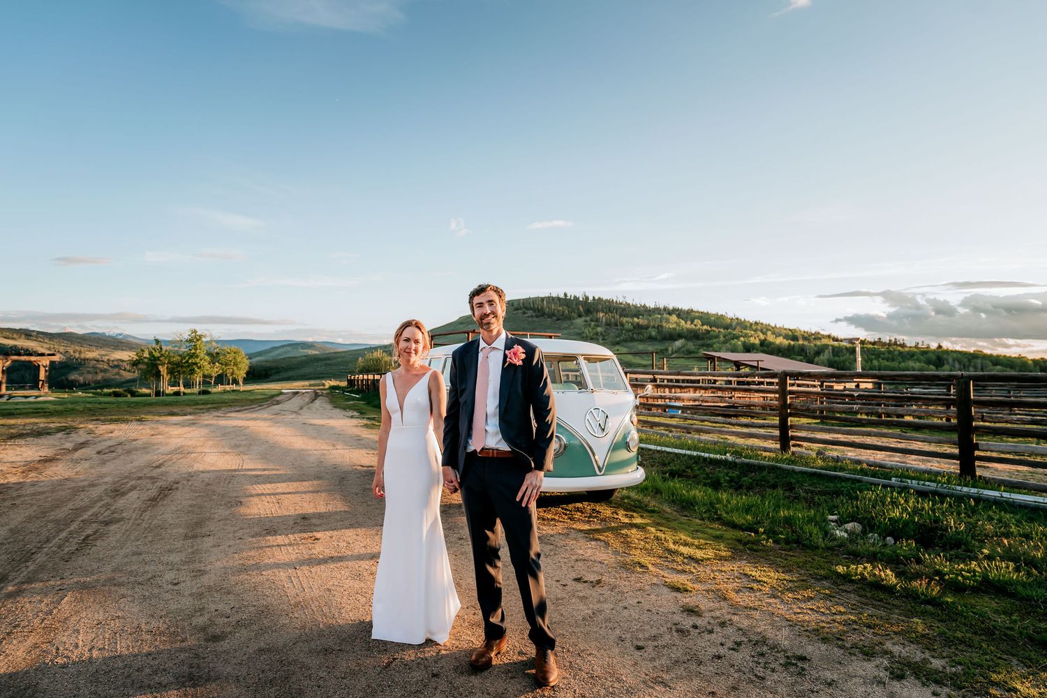 A wedding couple walks along a country road with their vintage VW bus in the background.